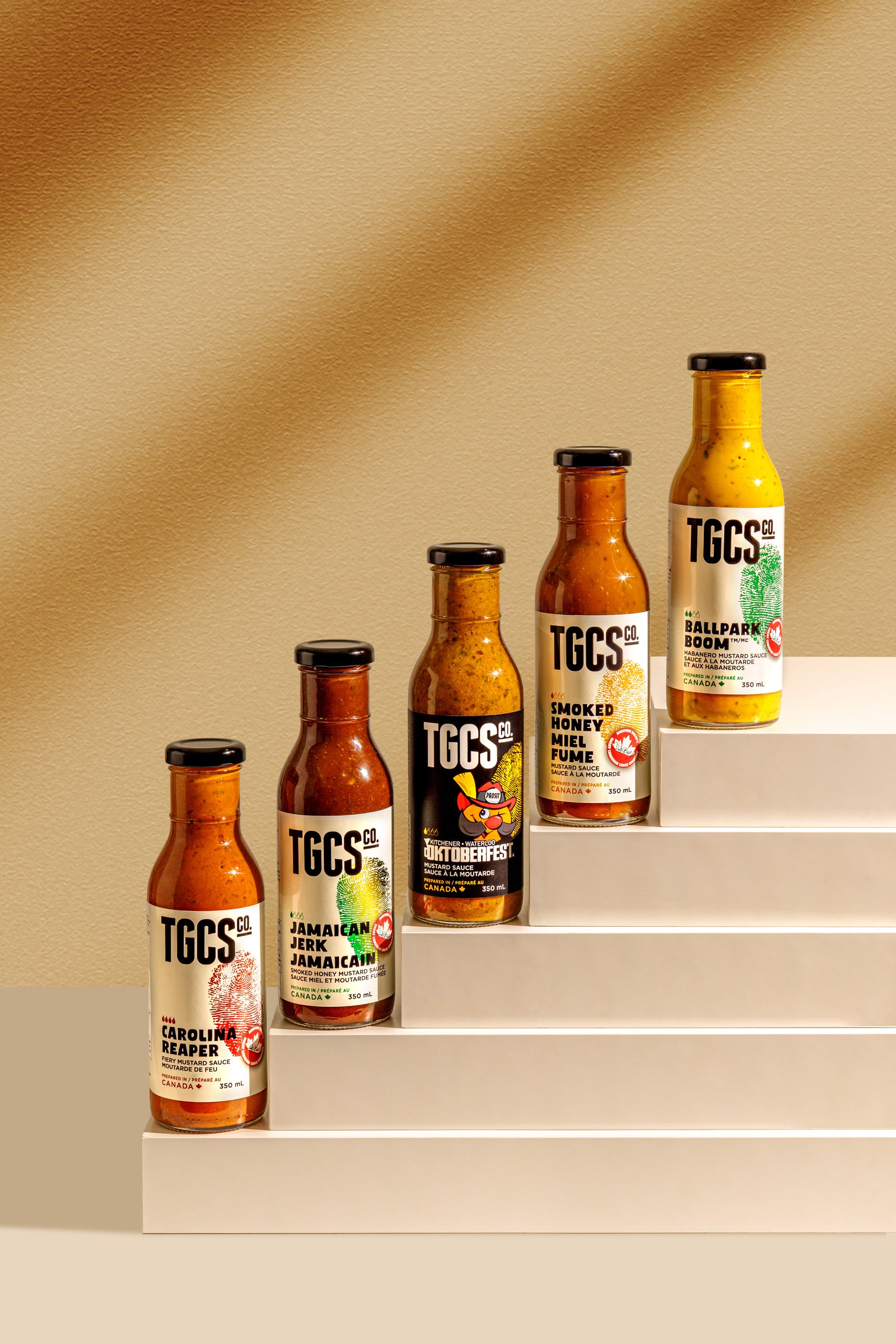 Collection of TGCS hot sauce bottles on a beige staircase